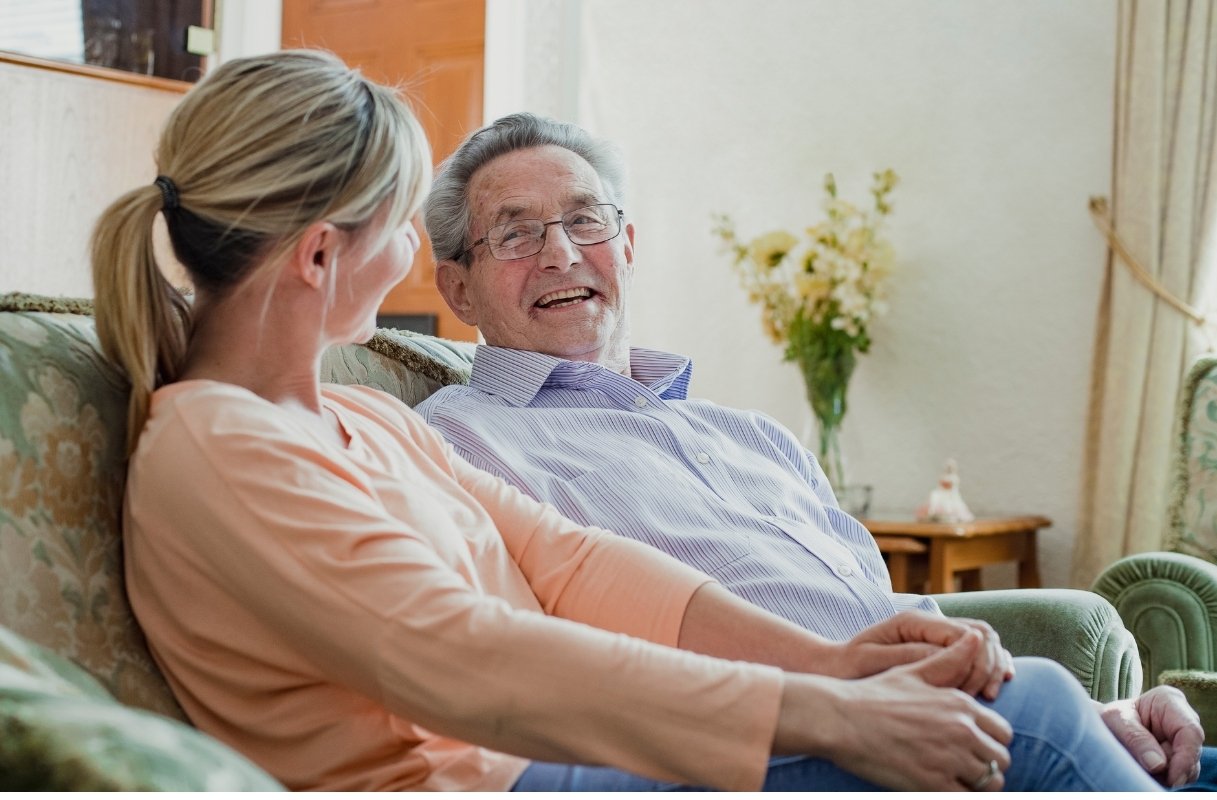 Companion chatting with an older man on the sofa at home